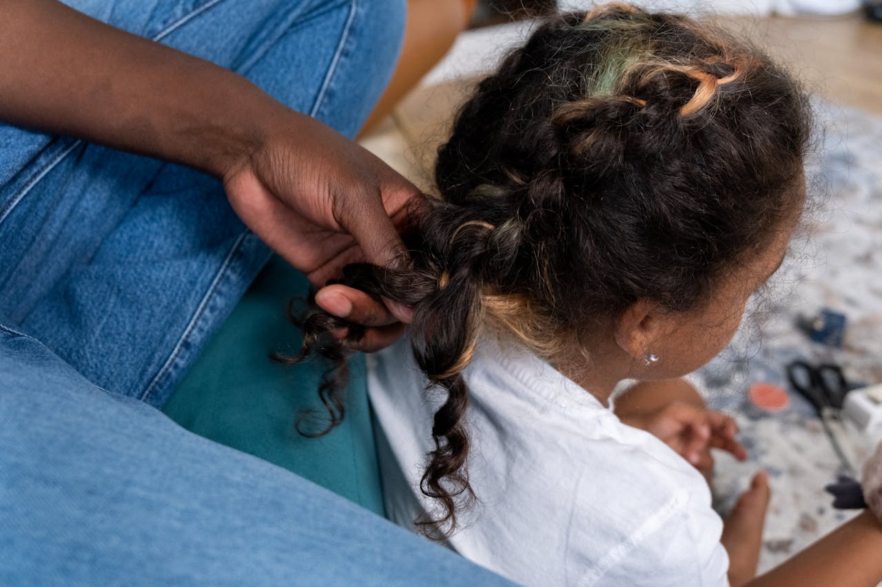 A close-up of a child's braided hair being styled by an adult's hand.